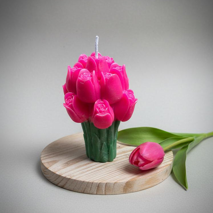 Pink tulip-shaped candle on a wooden stand with a gray background